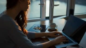 Une femme travaillant sur son ordinateur portable devant une fenêtre.