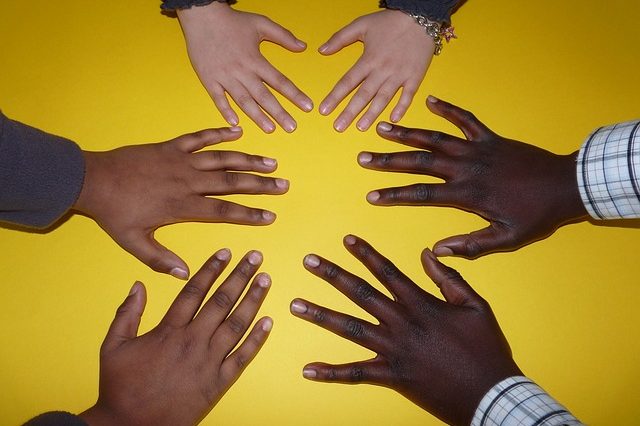 Cinq mains de différentes teintes de peau disposées en cercle sur un fond jaune, symbolisant l'esprit de travail d'équipe et renforçant l'unité au sein de l'entreprise.