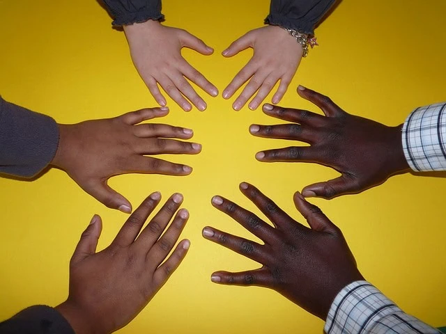 Cinq mains de différentes teintes de peau disposées en cercle sur un fond jaune, symbolisant l'esprit de travail d'équipe et renforçant l'unité au sein de l'entreprise.