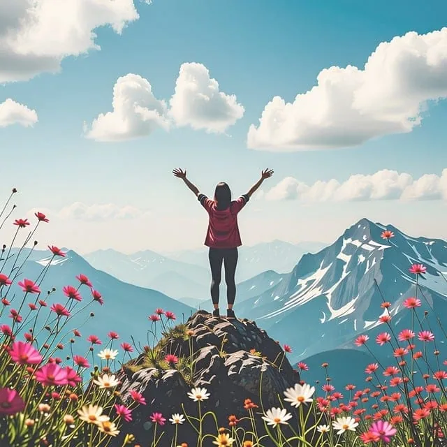 Une personne se tient sur un rocher, les bras levés, entourée de fleurs en fleurs, surplombant des montagnes enneigées sous un ciel bleu avec des nuages épars.