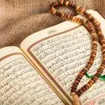 Un Coran ouvert avec un texte arabe est exposé avec un tasbih (chapelet de prière) en bois marron drapé dessus, posé sur un tissu en toile de jute - un cadeau idéal pour l'Aïd el-Fitr.