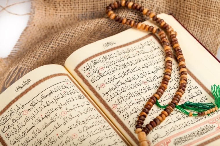 Un Coran ouvert avec un texte arabe est exposé avec un tasbih (chapelet de prière) en bois marron drapé dessus, posé sur un tissu en toile de jute - un cadeau idéal pour l'Aïd el-Fitr.