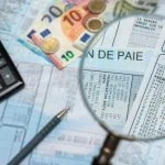 Une loupe agrandit les détails d'une fiche de paie, entourée d'une calculatrice, d'un stylo et de divers billets et pièces en euros. La scène souligne l'importance de l'IA dans la gestion de la paie, combinée à l'expertise humaine pour garantir l'exactitude et l'efficacité.