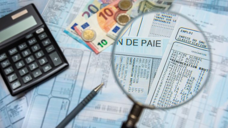 Une loupe agrandit les détails d'une fiche de paie, entourée d'une calculatrice, d'un stylo et de divers billets et pièces en euros. La scène souligne l'importance de l'IA dans la gestion de la paie, combinée à l'expertise humaine pour garantir l'exactitude et l'efficacité.