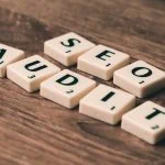 Les tuiles de Scrabble portant l'inscription « AUDIT SEO » sont soigneusement disposées sur une surface en bois, soulignant l'importance de réaliser un audit SEO efficace pour des performances Internet optimales du site.