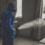 Personne portant un équipement de protection bleu utilisant une machine à brouillard à l'intérieur.