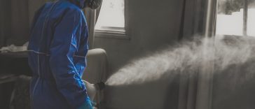 Personne portant un équipement de protection bleu utilisant une machine à brouillard à l'intérieur.