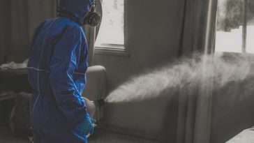 Personne portant un équipement de protection bleu utilisant une machine à brouillard à l'intérieur.