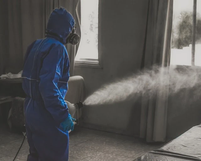 Personne portant un équipement de protection bleu utilisant une machine à brouillard à l'intérieur.