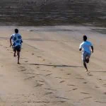 Deux amis, liés par l'amitié, courent le long d'une plage de sable, laissant derrière eux des empreintes de pas.