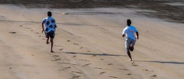 Deux amis, liés par l'amitié, courent le long d'une plage de sable, laissant derrière eux des empreintes de pas.