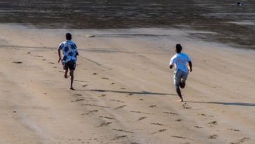 Deux amis, liés par l'amitié, courent le long d'une plage de sable, laissant derrière eux des empreintes de pas.